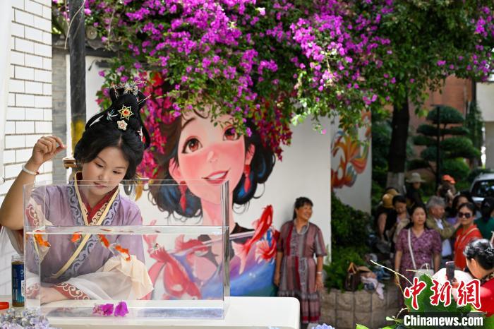 「花で髪を飾った少女」が描かれた壁の前にある水槽の金魚に餌をあげる女性（6月5日撮影?李嘉嫻）。